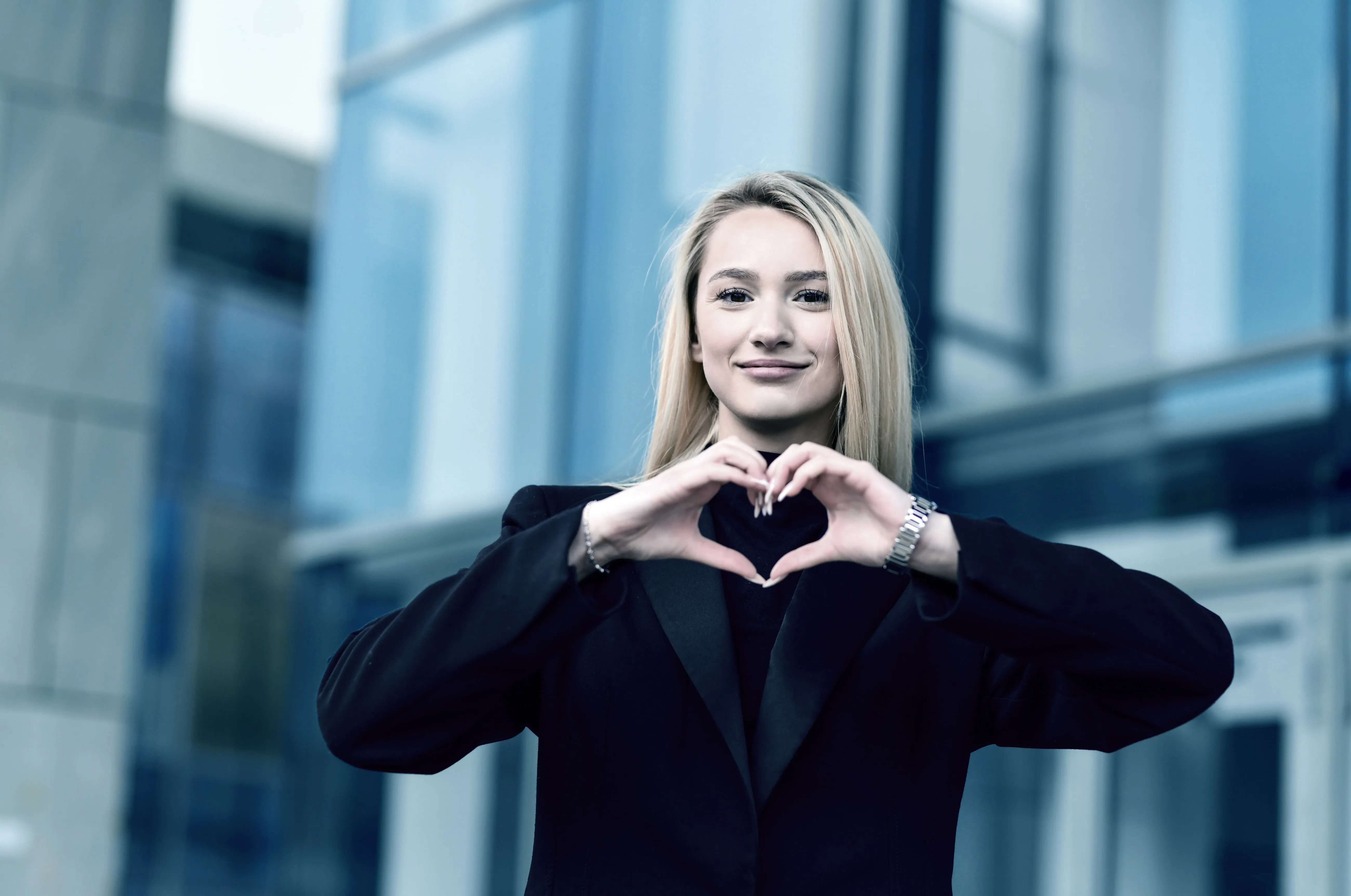 A client outside a glass office building, making a heart with her hands